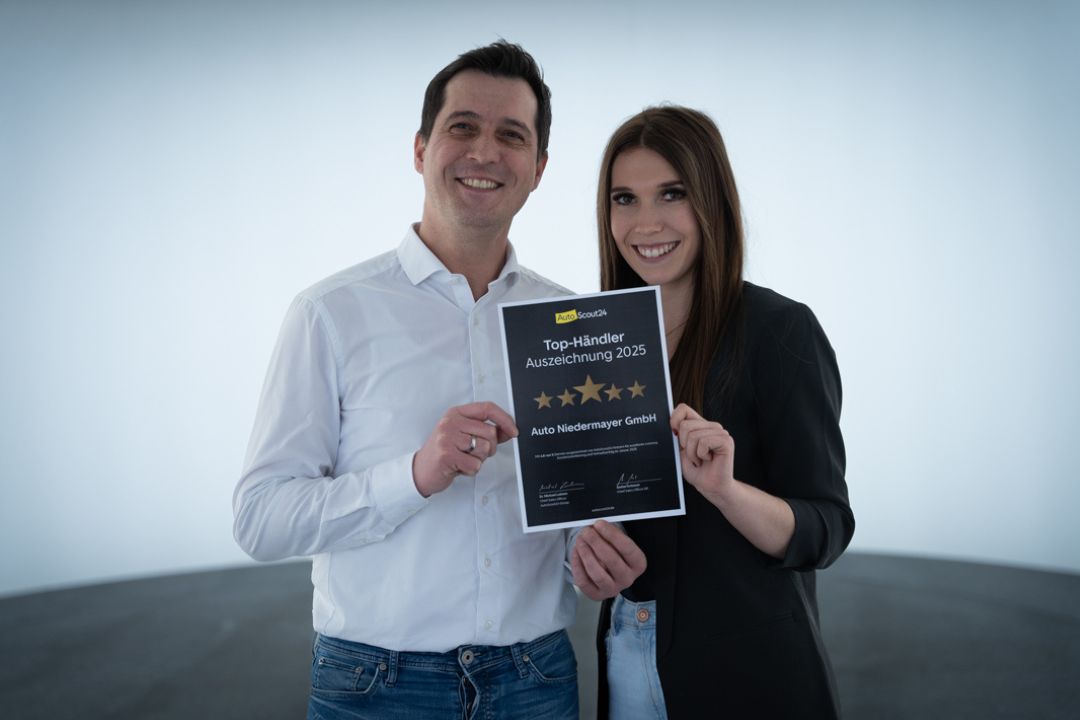 zu sehen sind zwei Mitarbeiter, die die AutoScout24 Top Händler 2025 in der Hand halten